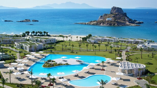 A resort with a large pool, palm trees, and a view of the sea and mountains.