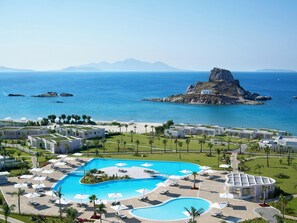 A resort with a large pool, palm trees, and a view of the sea and mountains.