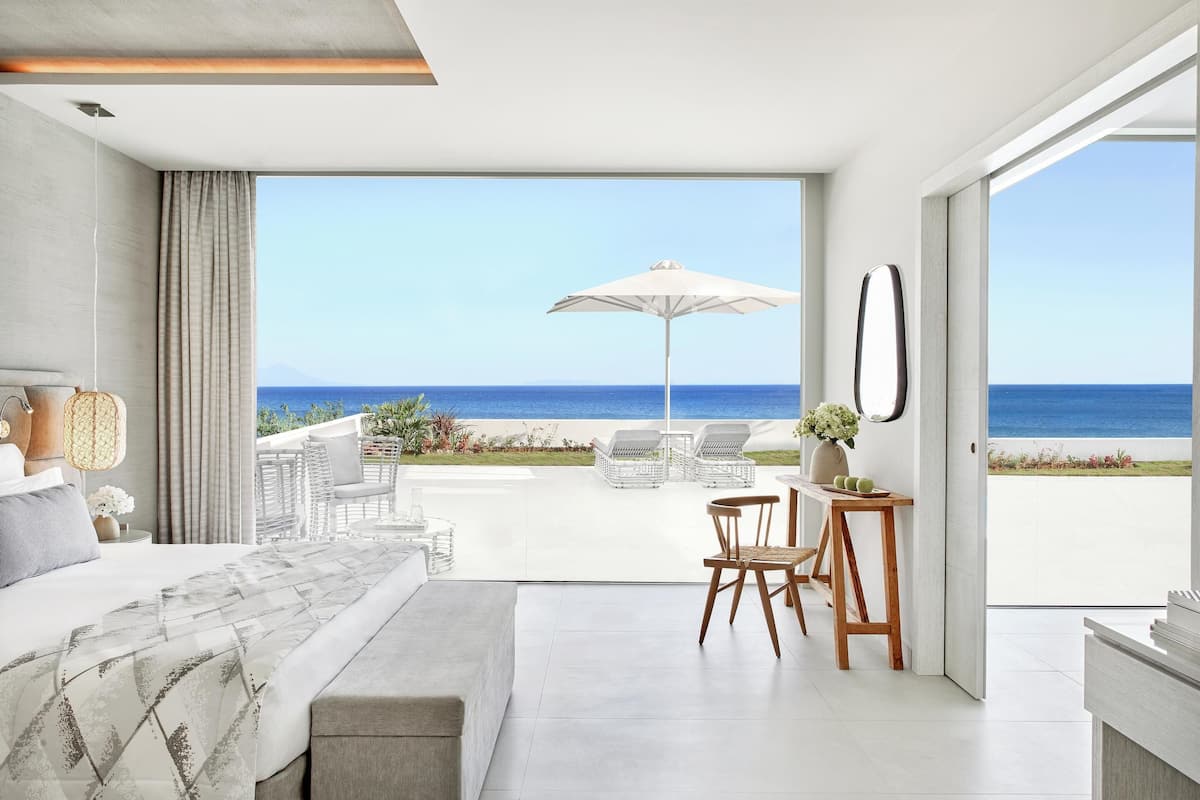 A modern bedroom with a large bed, a desk, and a view of the beach.