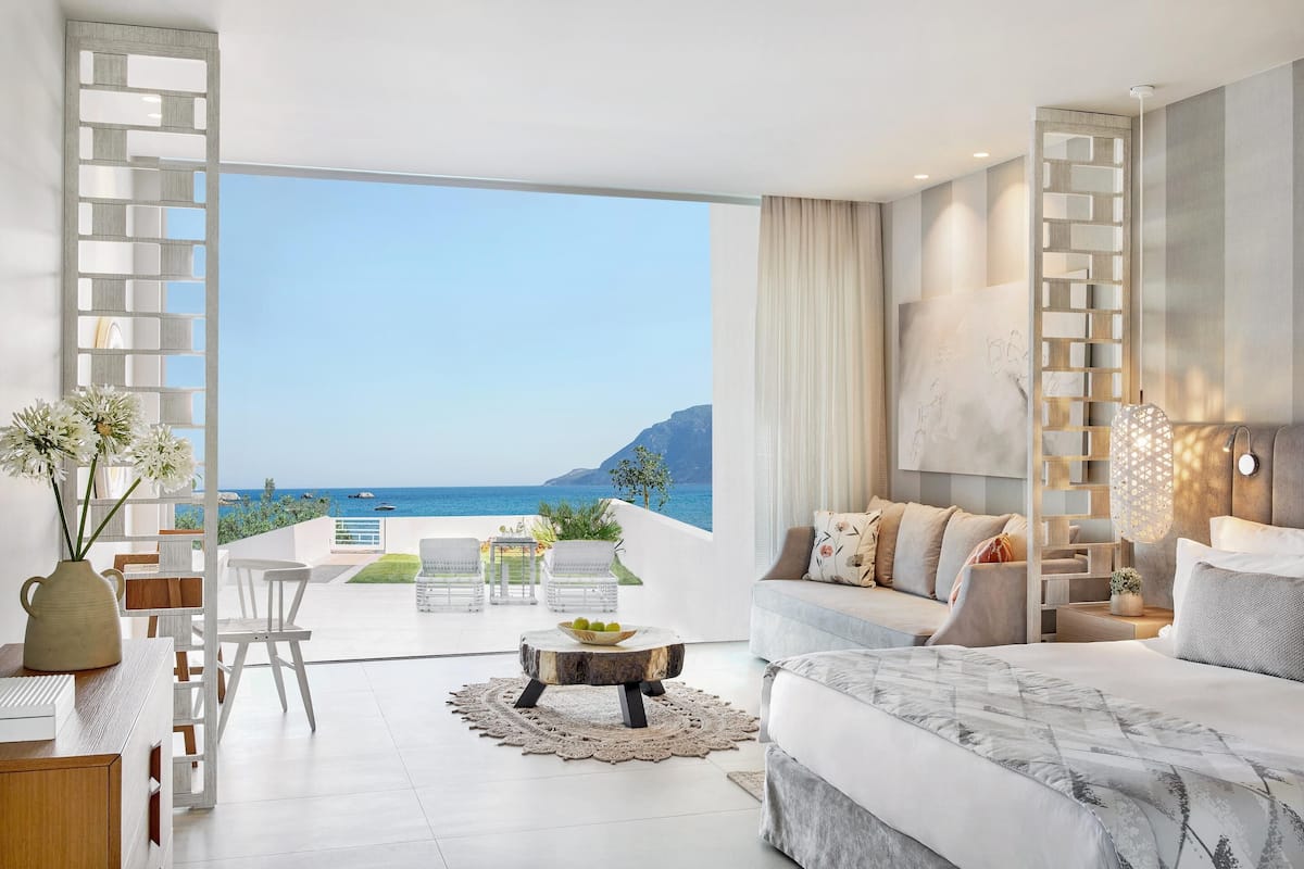 A modern bedroom with a large bed, a sofa, and a dining area with a view of the sea.