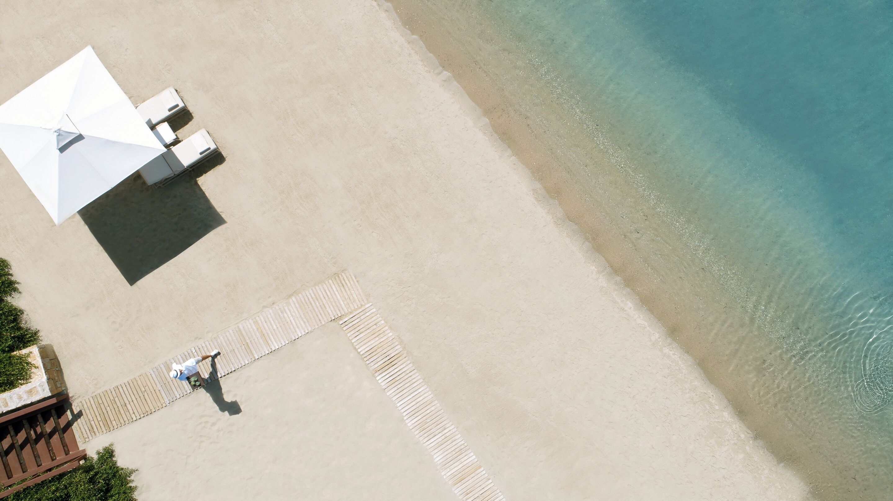 An aerial view of a beach with a pathway leading to a seating area with umbrellas.