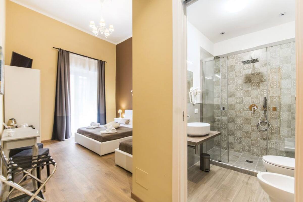 Ein modernes Hotelzimmer mit Bett, Nachttisch und einer Duschkabine mit Glastür.