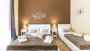 Habitación de hotel con dos camas, cada una con cubrecama marrón y almohadas blancas. Se observan mesitas de noche con lámparas y una obra de arte en la pared sobre las camas.