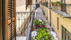 Una calle estrecha flanqueada por edificios, con balcones adornados con plantas y flores.