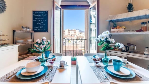 Un área de desayuno con vista a edificios, un menú en una pizarra y un balcón con plantas.