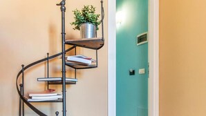 Una estantería metálica en espiral con libros y una planta en maceta, apoyada en una pared.