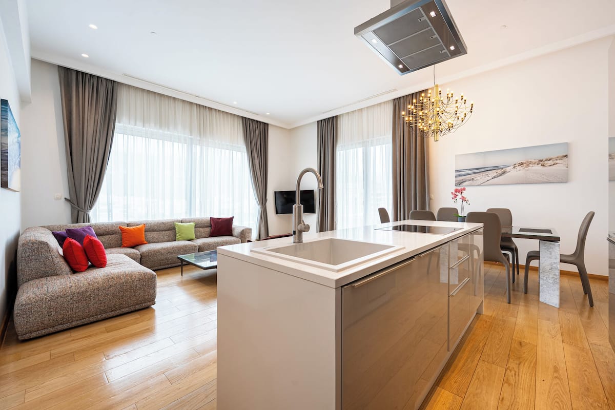 A modern living room with a sofa, a dining area, and a kitchen island with a sink.