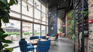 A restaurant with large windows, blue chairs, wooden tables, and a brick wall with a wine rack. - Hotel Wow (Budva)