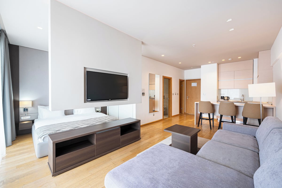 A modern hotel room with a bed, TV, sofa, and a small dining area.