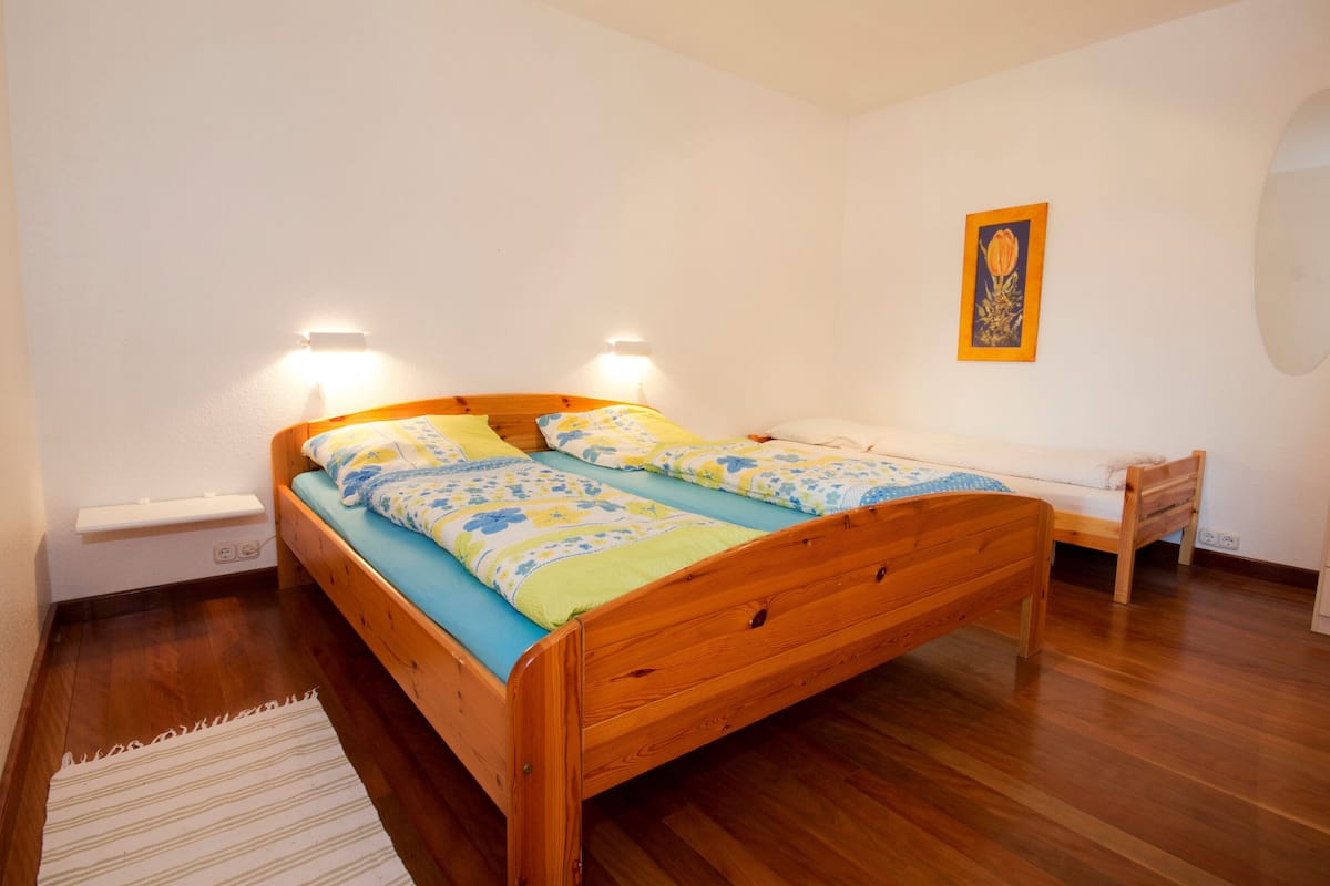 A bedroom with a wooden bed, a bedside table, a chair, and a small desk.