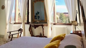 A room with a wooden ceiling, a bed with a white and blue striped bedspread, a yellow pillow, and a large mirror on a wooden dresser. - B&B Paolina (Siena)