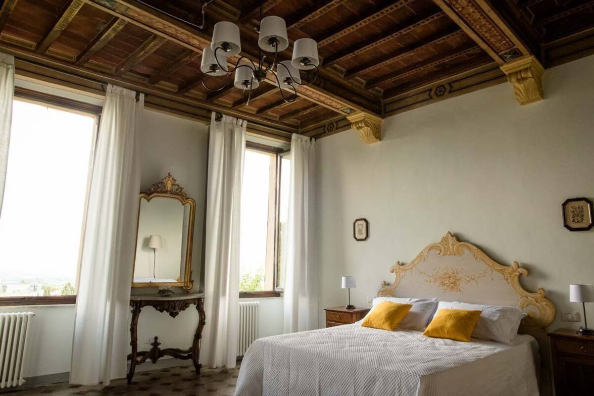 A bedroom with a large bed, a wooden ceiling, and a window with curtains.