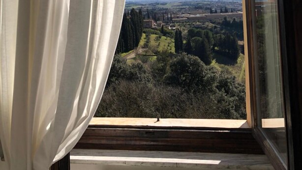 A window with a view of a landscape, including trees and a distant town. - B&B Paolina (Siena)