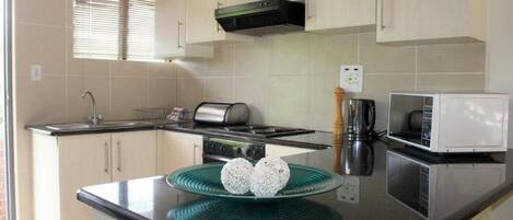 A modern kitchen with light-colored cabinets, a stainless steel stove, a microwave, and a green glass serving tray with two white items.