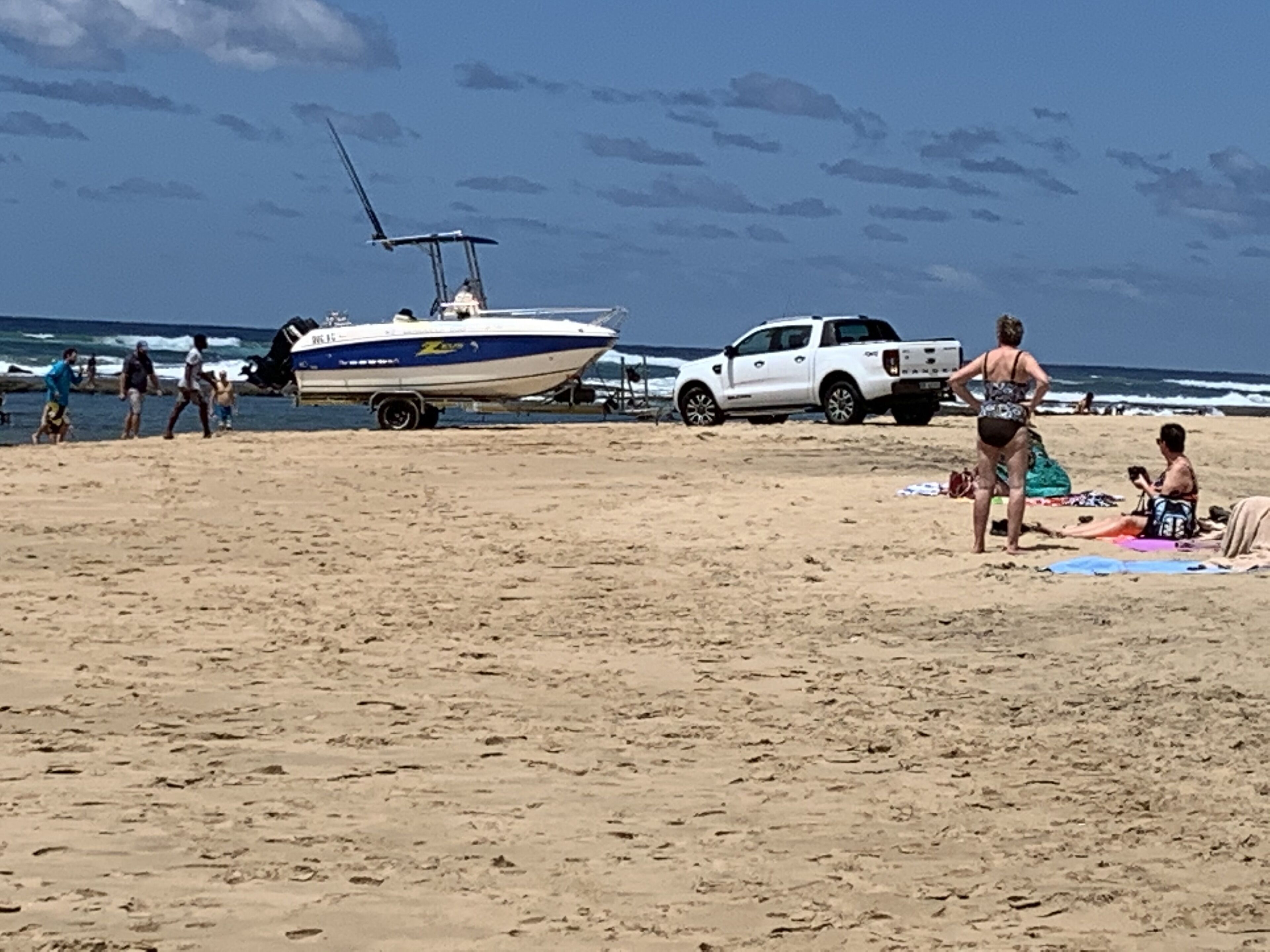A beach with a boat, a white truck, and people.