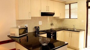A modern kitchen with light wooden cabinets, a black countertop, a microwave, a coffee maker, and a sink. - Flamingo Lodge (St. Lucia)