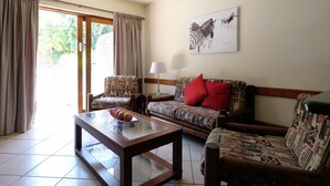 A living room with patterned furniture, a glass coffee table, and a zebra artwork on the wall. - Flamingo Lodge (St. Lucia)