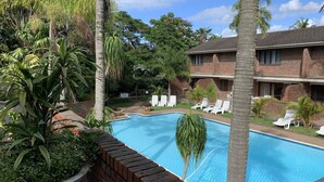 A swimming pool surrounded by palm trees and a brick building with white lounge chairs. - Flamingo Lodge (St. Lucia)