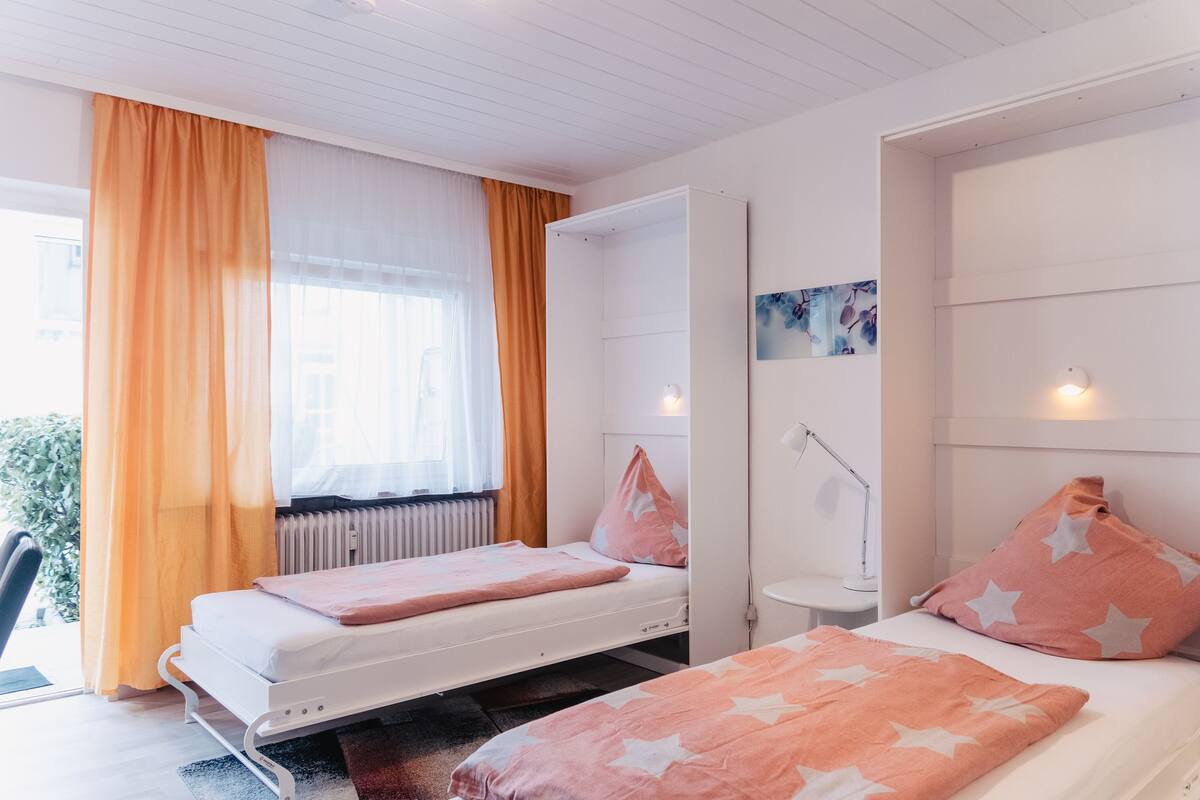 Un dormitorio con dos camas, un radiador, un escritorio con lámpara y una ventana con cortinas.