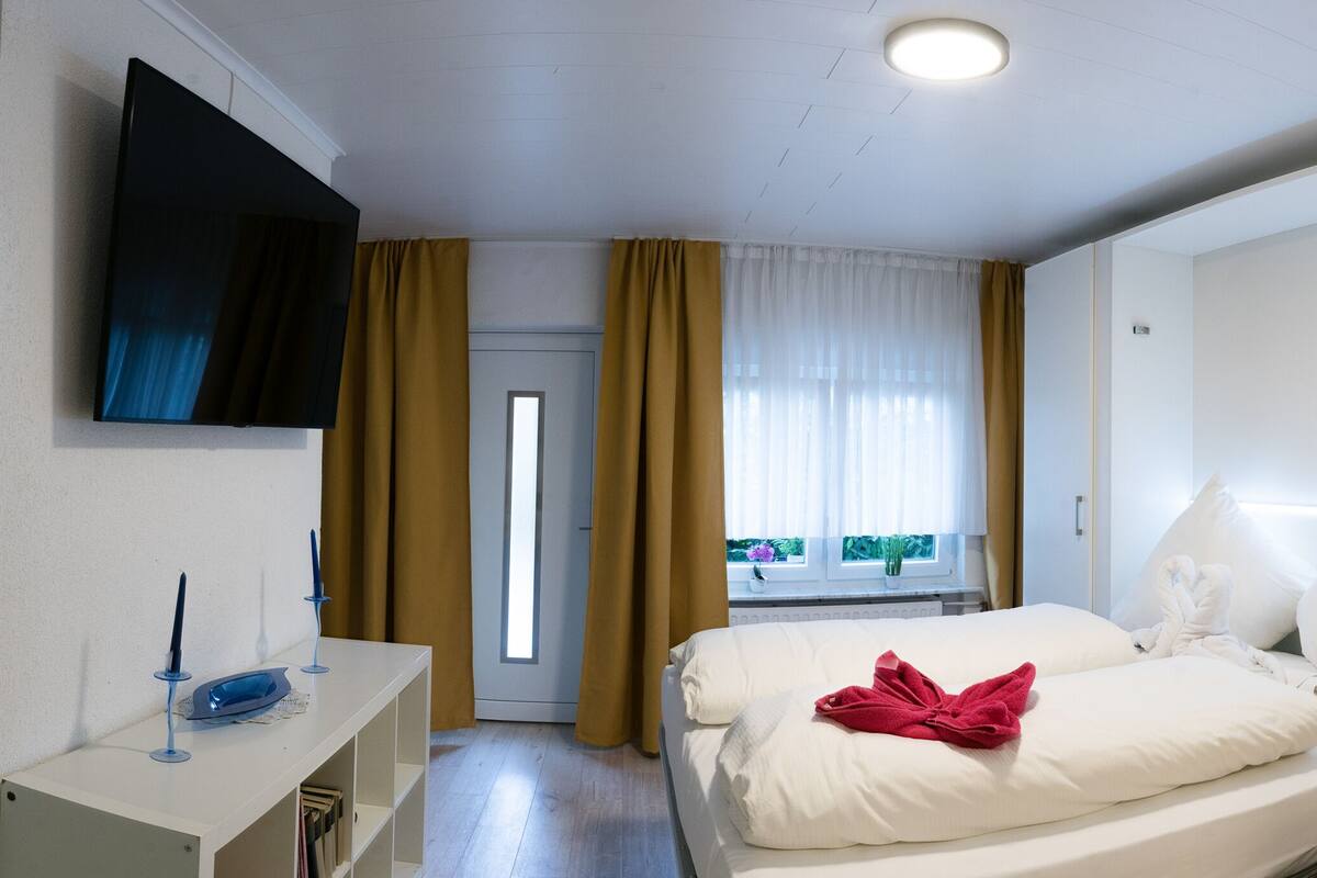 Habitación de hotel con cama, escritorio con televisor de pantalla plana, ventana con cortinas y puerta.