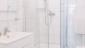 Un baño moderno con ducha de vidrio, azulejos blancos, un lavamanos blanco y un inodoro.
