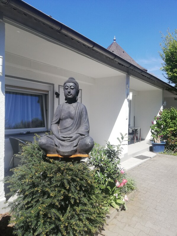 Una estatua de Buda en un jardín, con un edificio blanco al fondo.
