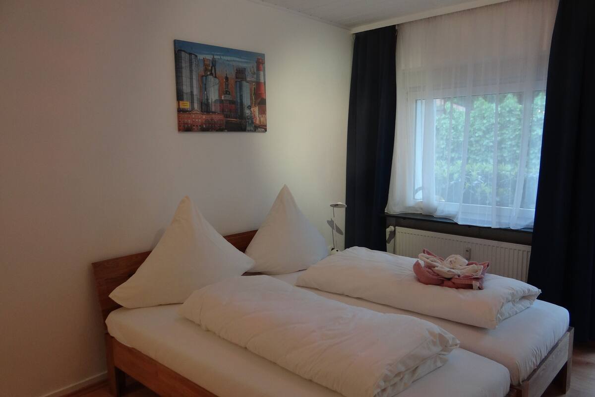 Una cama doble con sábanas y almohadas blancas, un cuadro en la pared y un ventanal con cortinas.