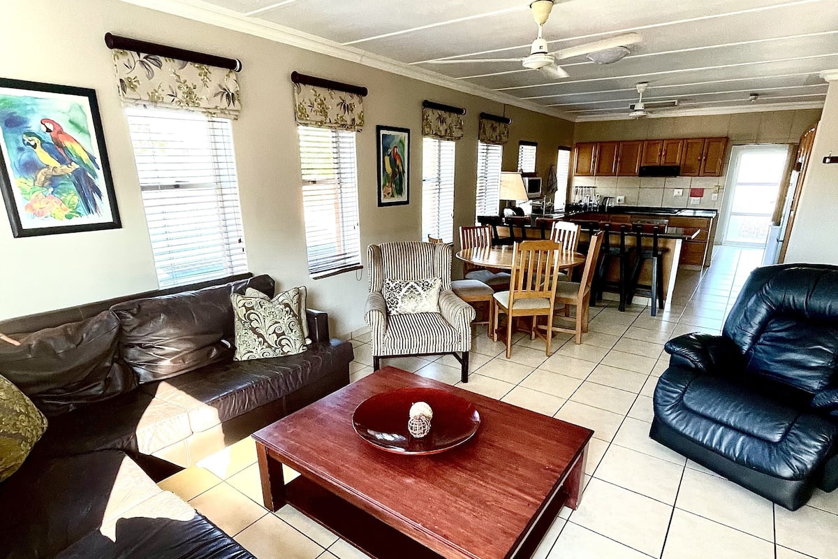 A living room with a sofa, a dining table, and a kitchen area in the background.