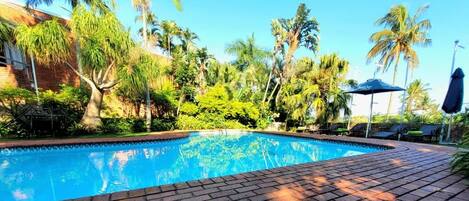 Una piscina con solárium de ladrillo, rodeada de palmeras y vegetación.