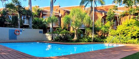 A swimming pool surrounded by palm trees and a brick building.