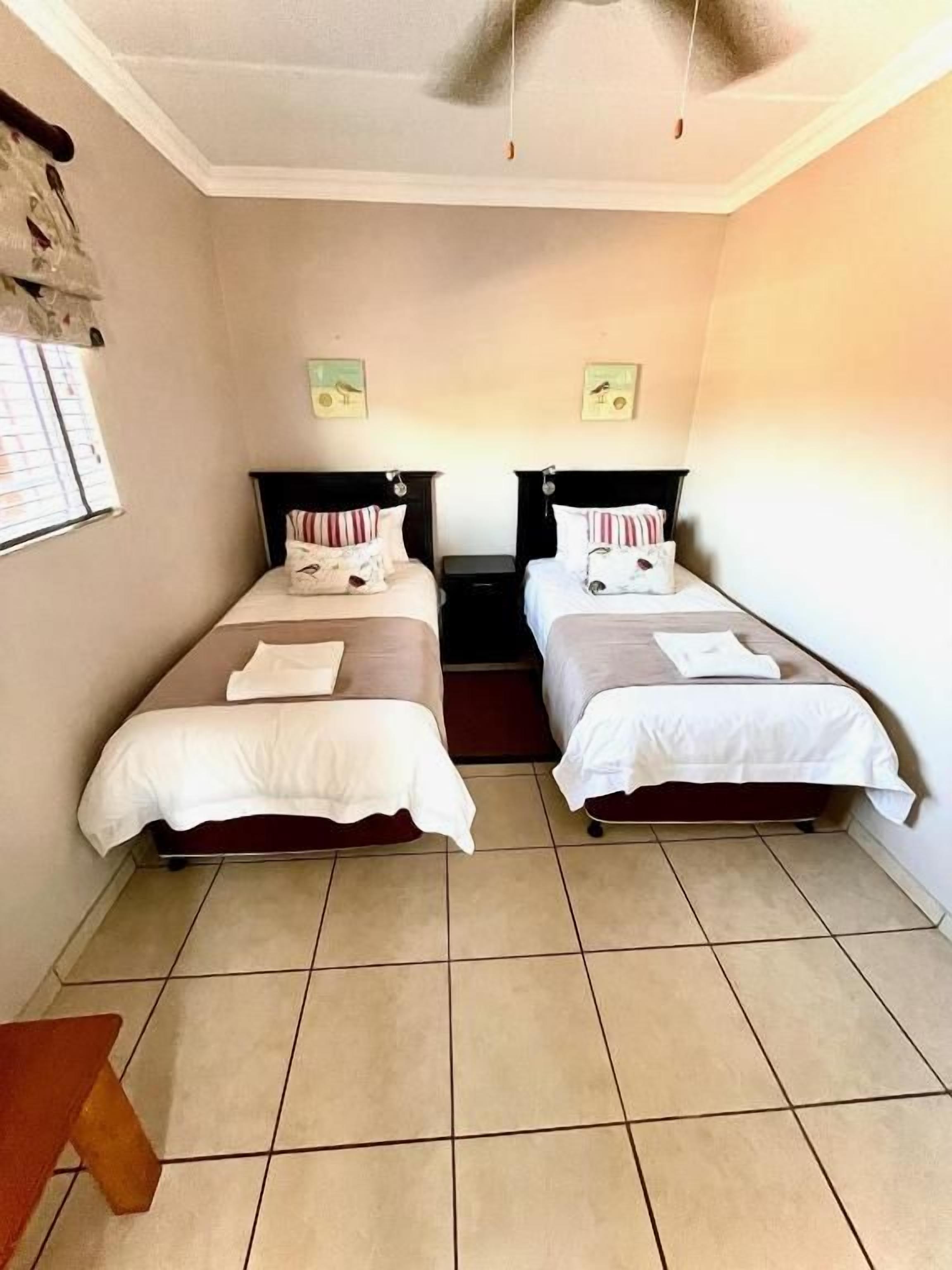 A room with two beds, a ceiling fan, and a small table.