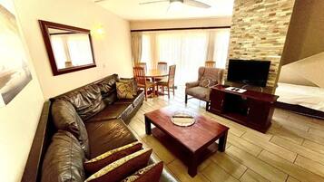 A living room with a leather sofa, a coffee table, a television, and a dining area with chairs and a table.