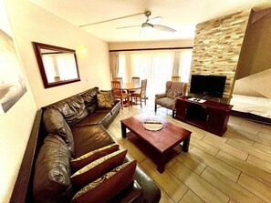 A living room with a leather sofa, a coffee table, a television, and a dining area with chairs and a table.