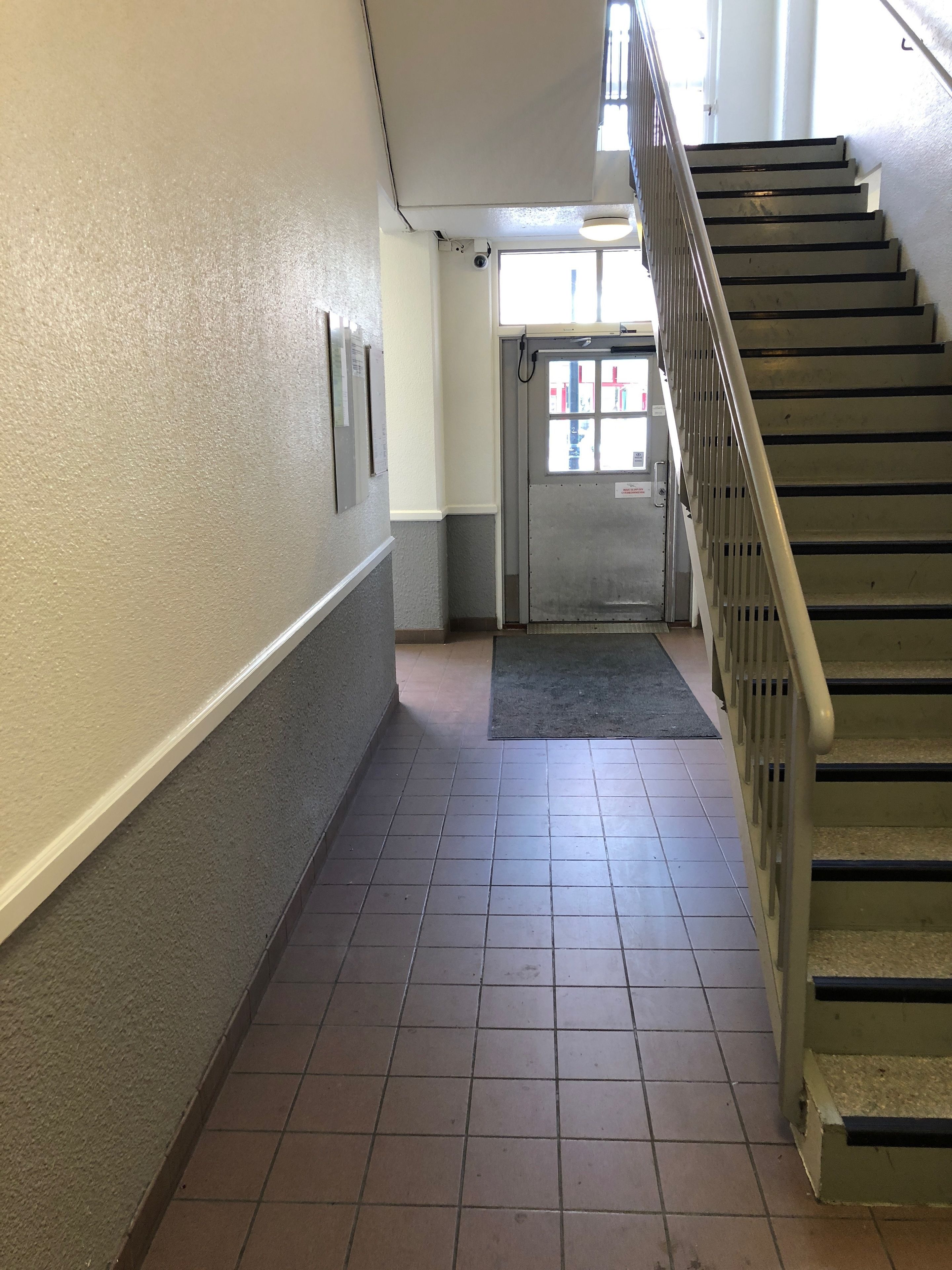 A hallway with a tiled floor, a metal staircase, and a door with a window.