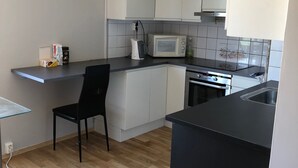 A compact kitchen with white cabinets, a microwave, a kettle, and a stove. There is a black chair and a glass table. - Guest House Centrum 3 (Oslo)