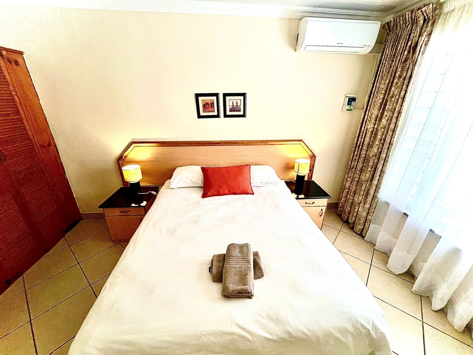 Habitación de hotel con una cama grande, dos mesitas de noche con lámparas, aire acondicionado de pared y cortinas.