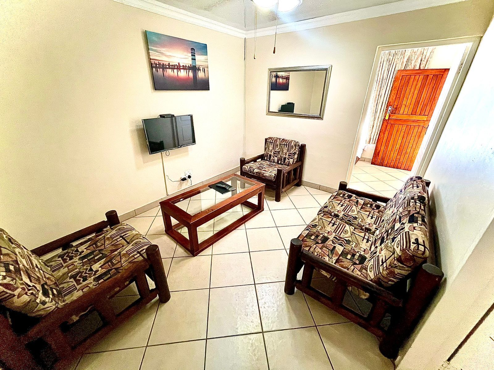 A living room with patterned sofas, a coffee table, a TV, and a mirror on the wall.