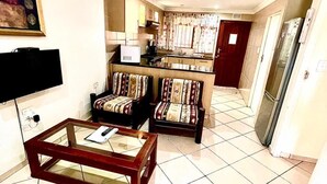 A living room with a TV, two sofas, a coffee table, and a kitchen area with a refrigerator. - St Lucia Palms (St. Lucia)