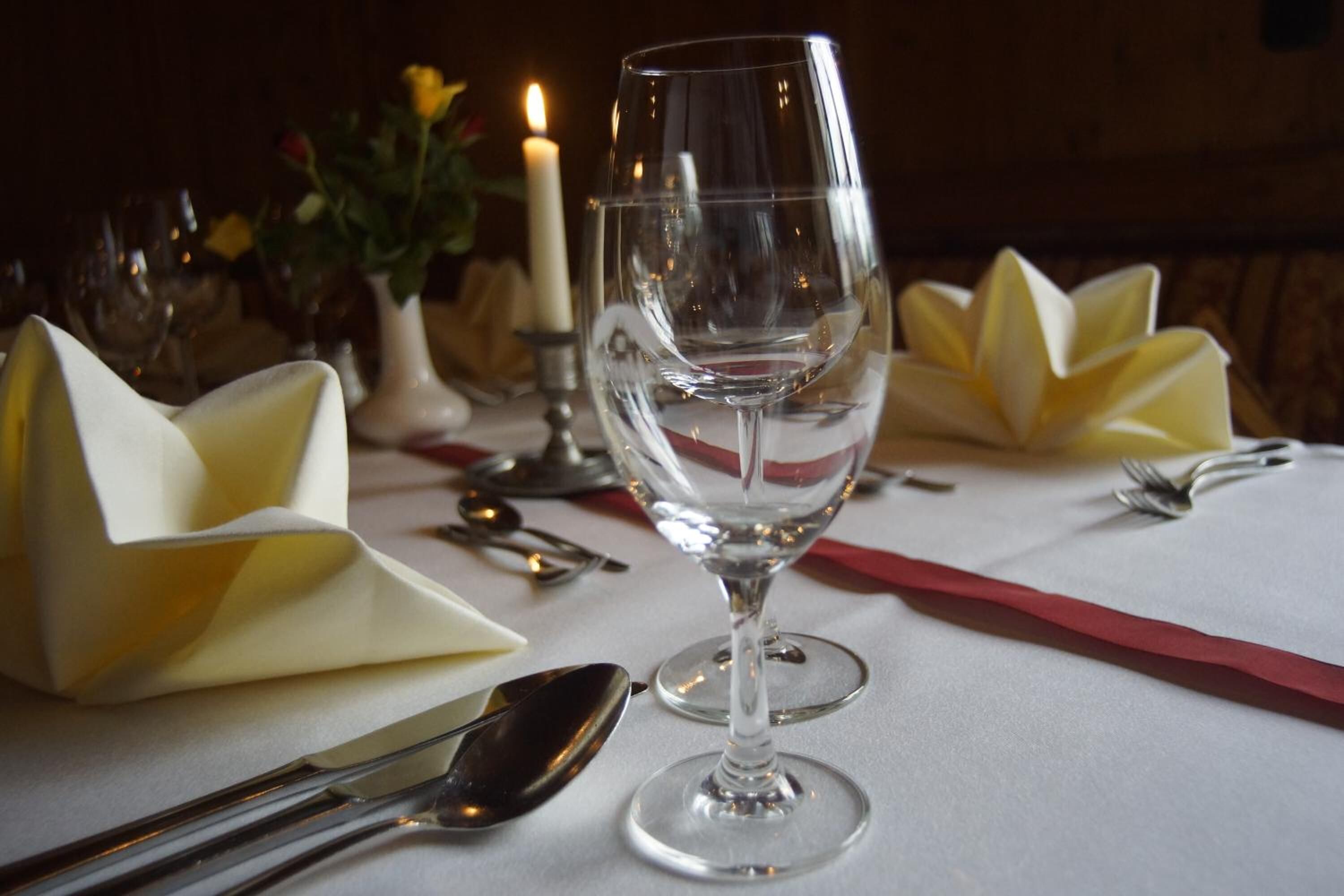 Una mesa lista para comer, con una copa de vino transparente, servilletas dobladas y cubiertos.