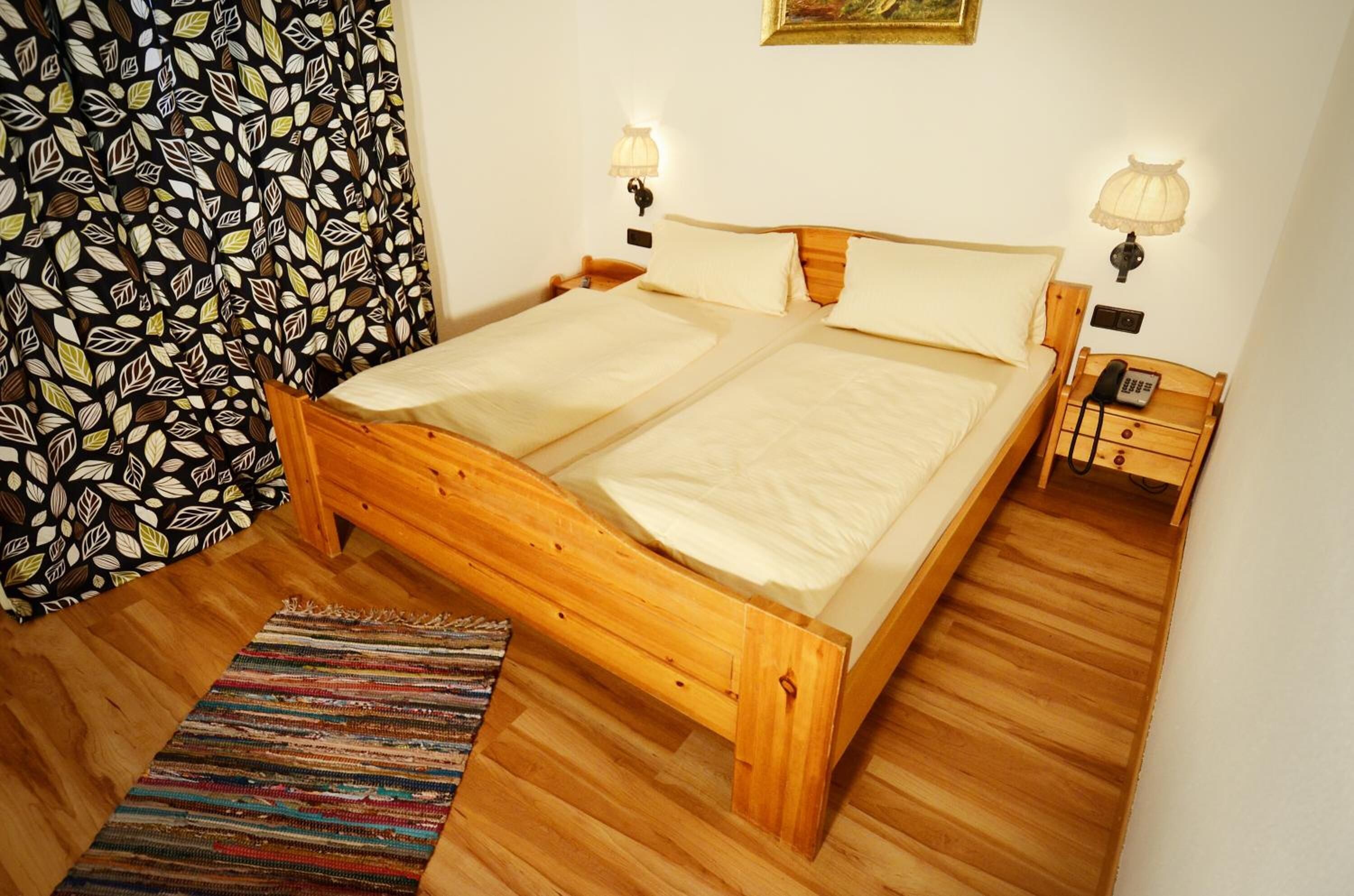 Ein Doppelbett mit hölzernem Kopfteil und Fußteil, zwei Nachttischlampen, ein Nachttischtelefon und ein gemustertes Vorhang.