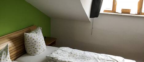 Un dormitorio con dos camas, cabeceros de madera, pared verde y ventana con toldo blanco.