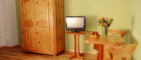 Een houten kast, een kleine tafel met een televisie, een stoel en een vaas met bloemen.