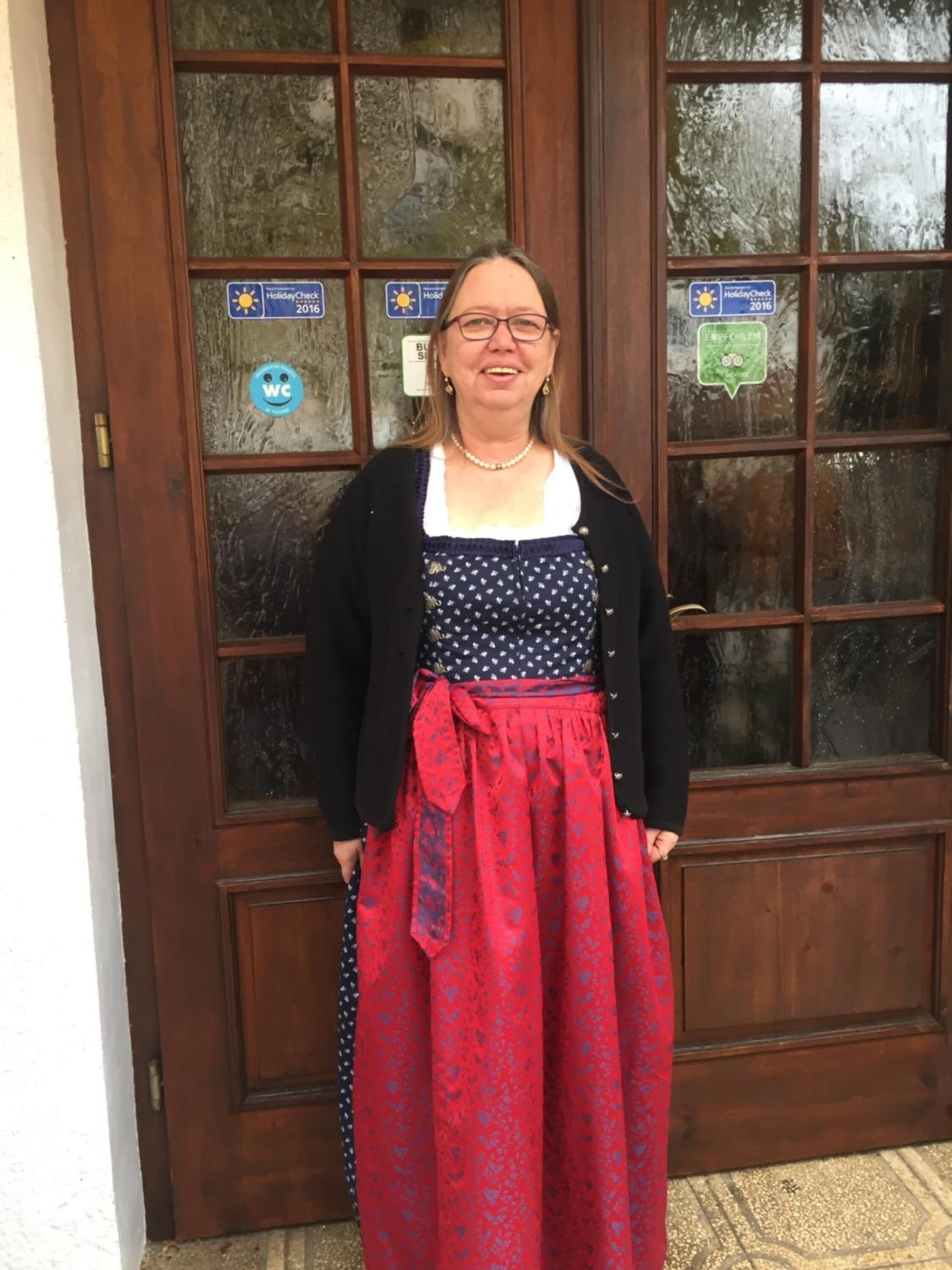 A person standing in front of a wooden door with glass panels, wearing a patterned dress and a cardigan.