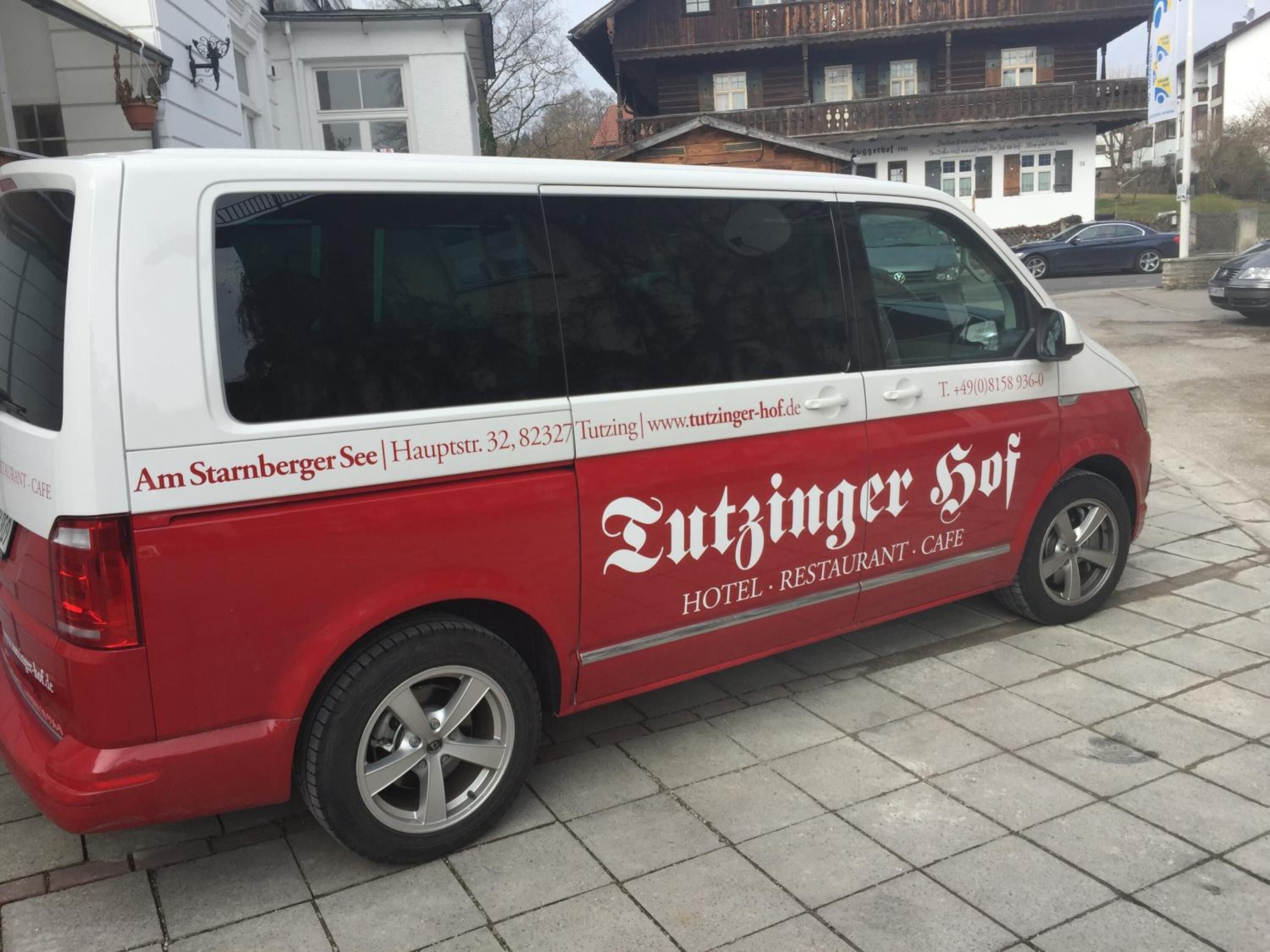 Una camioneta roja y blanca con la marca "Tutzinger Hof", estacionada en una zona pavimentada.