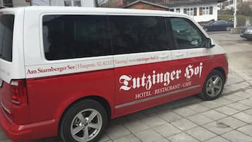 Un fourgon rouge et blanc arborant le logo « Tutzinger Hof », garé sur une surface pavée.