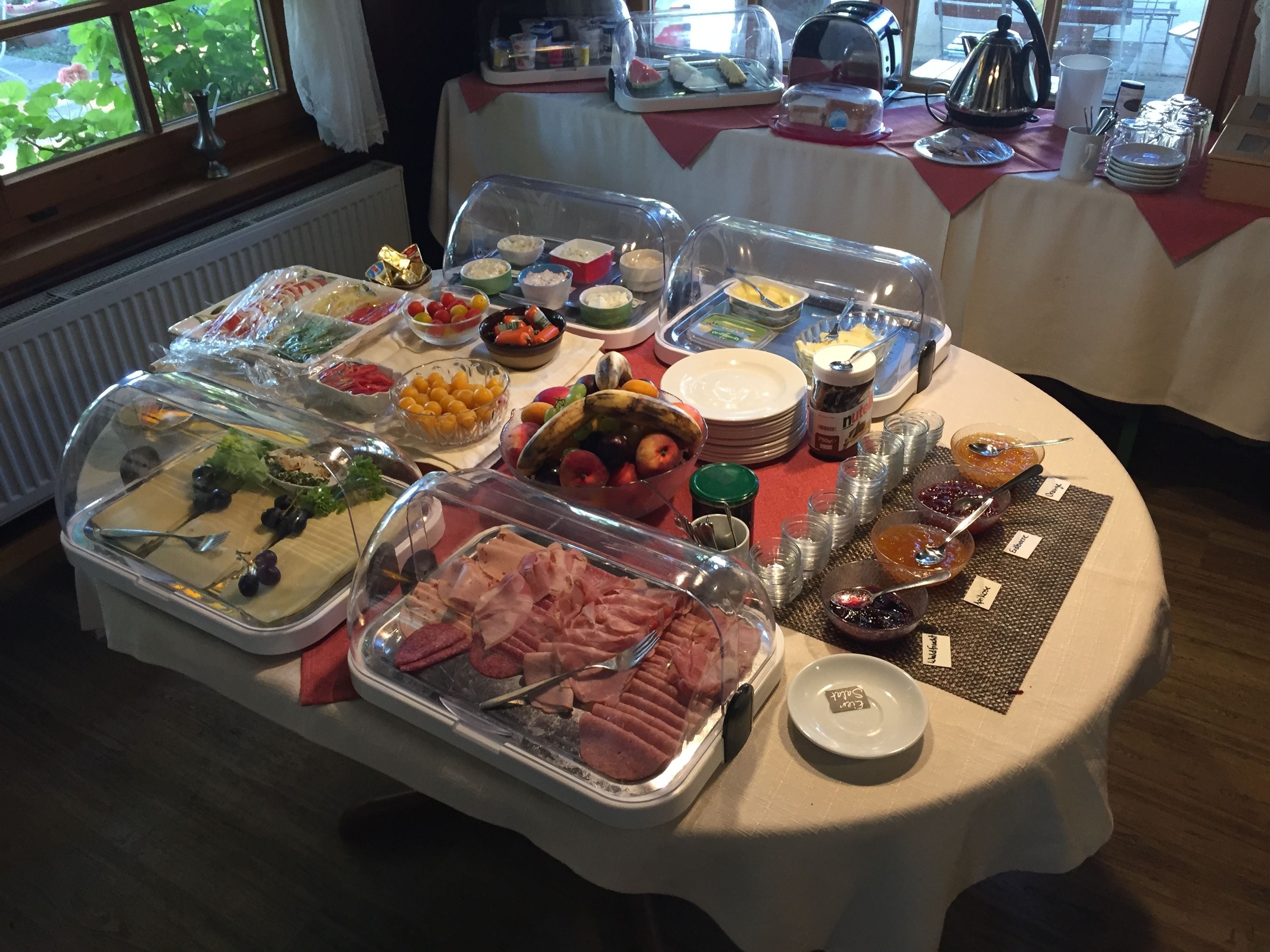 A buffet table with various food items, including fruits, cheeses, and meats, covered with clear plastic domes.