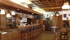 Zona de bar con mostradores de madera, varios taburetes e iluminación colgante.