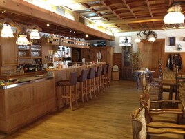 Uma área de bar com balcões de madeira, vários bancos e luminárias pendentes.