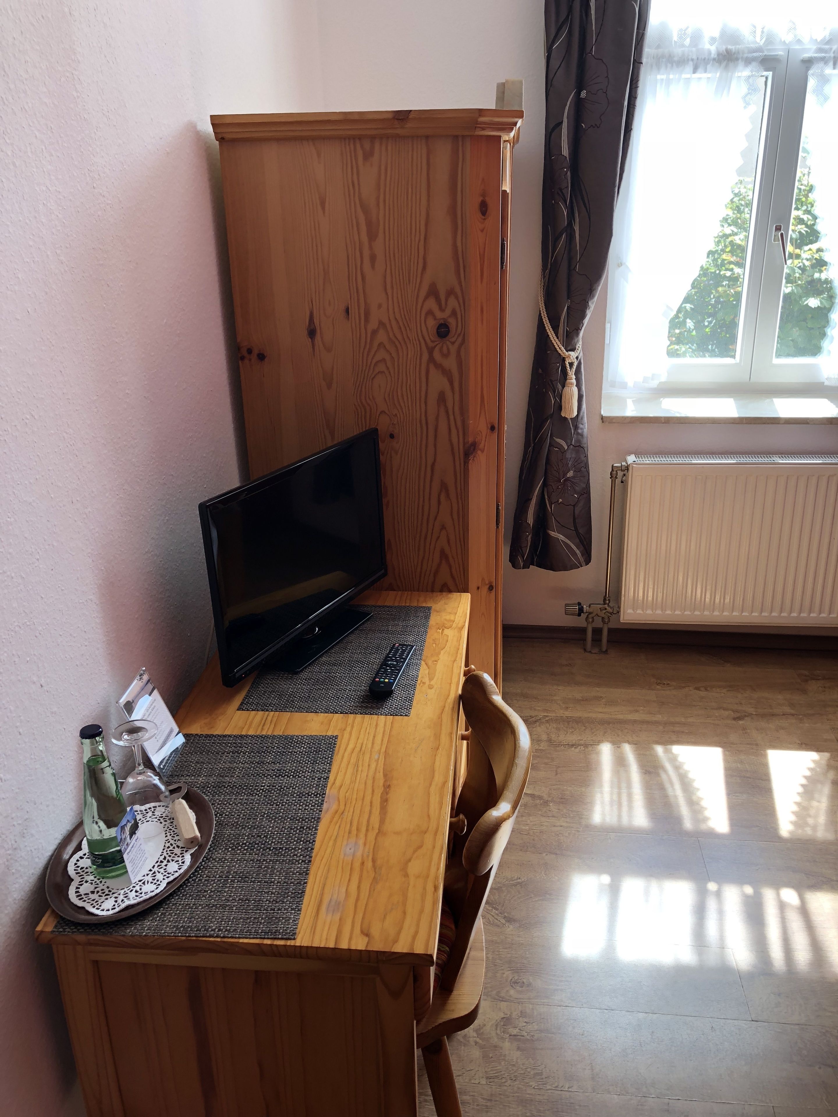 Een houten bureau met een laptop, een afstandsbediening en een glas met een fles.