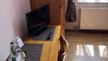 Een houten bureau met een laptop, een afstandsbediening en een glas met een fles.